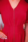 A vibrant red tinsley zipper dress featuring a gold front zipper and smocked waistband in a v-neck style
